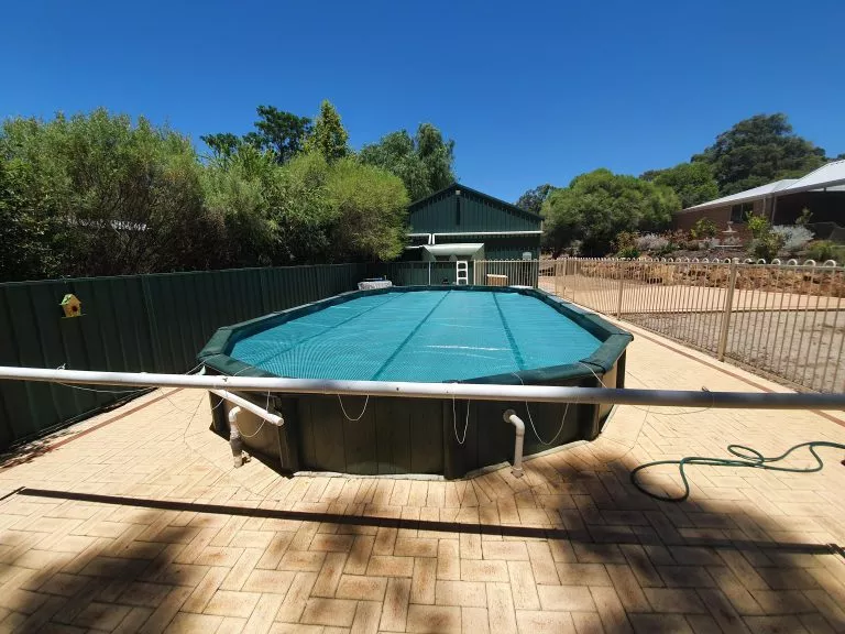 AGA Roller set up behind above ground pool with 525 Titanium Green Solar Cover.